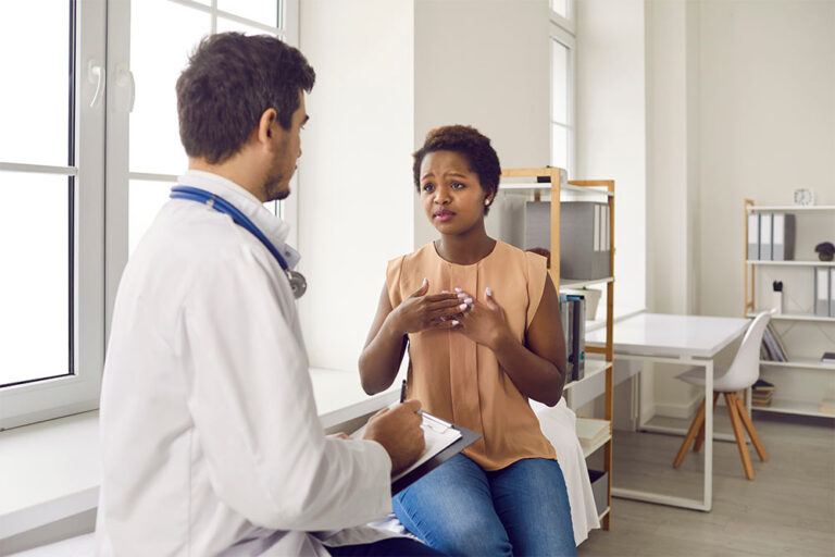 a doctor in a white lab coat speaks to a female patient in a brown shirt in a hospital setting
