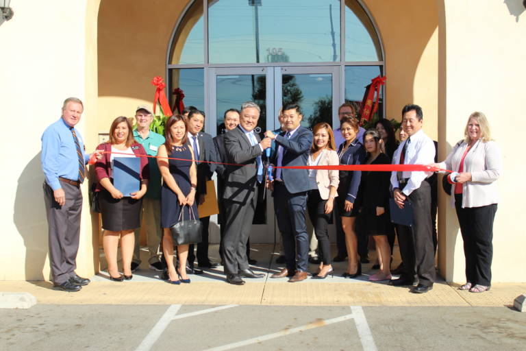 a group of people holding a red ribbon while two men in the center hold a pair of giant scissors