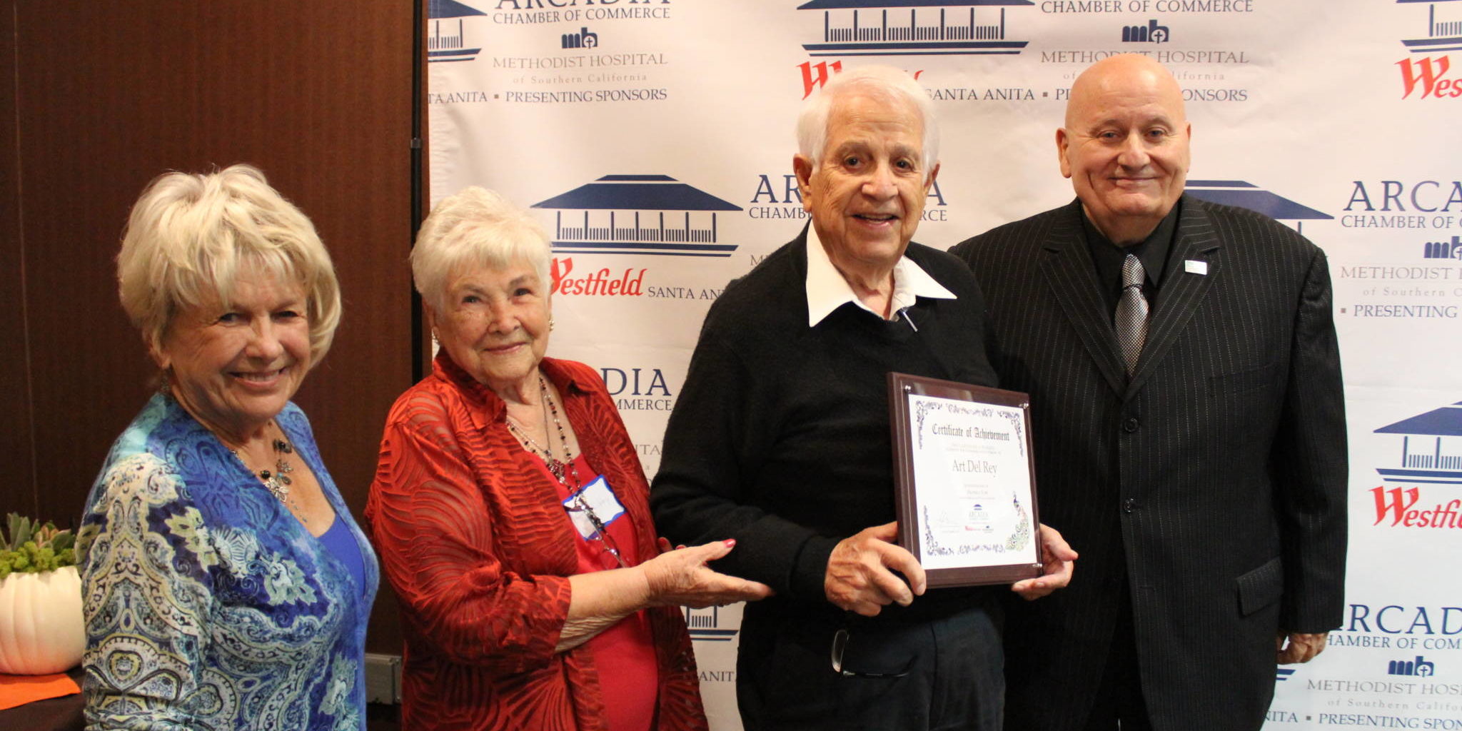 two women present a man with a plaque while another man in a suit stands beside them