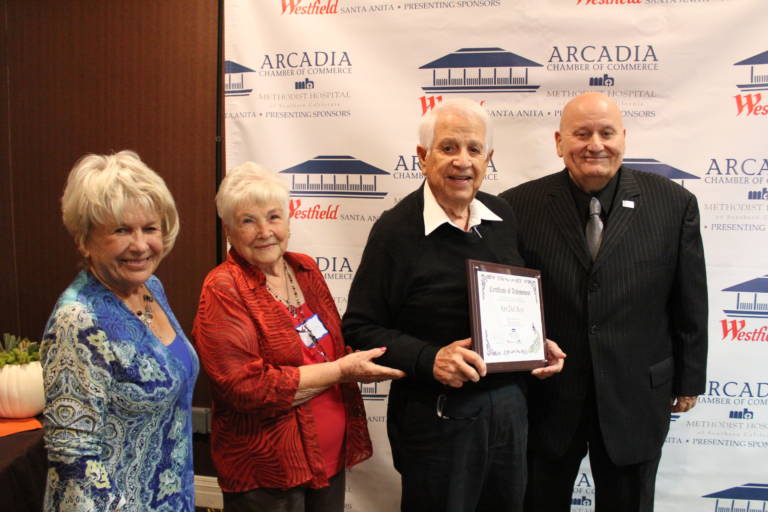 two women present a man with a plaque while another man in a suit stands beside them