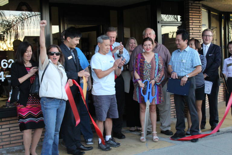 a group of people stands beside a woman holding a large pair of scissors and there is a cut ribbon on the ground