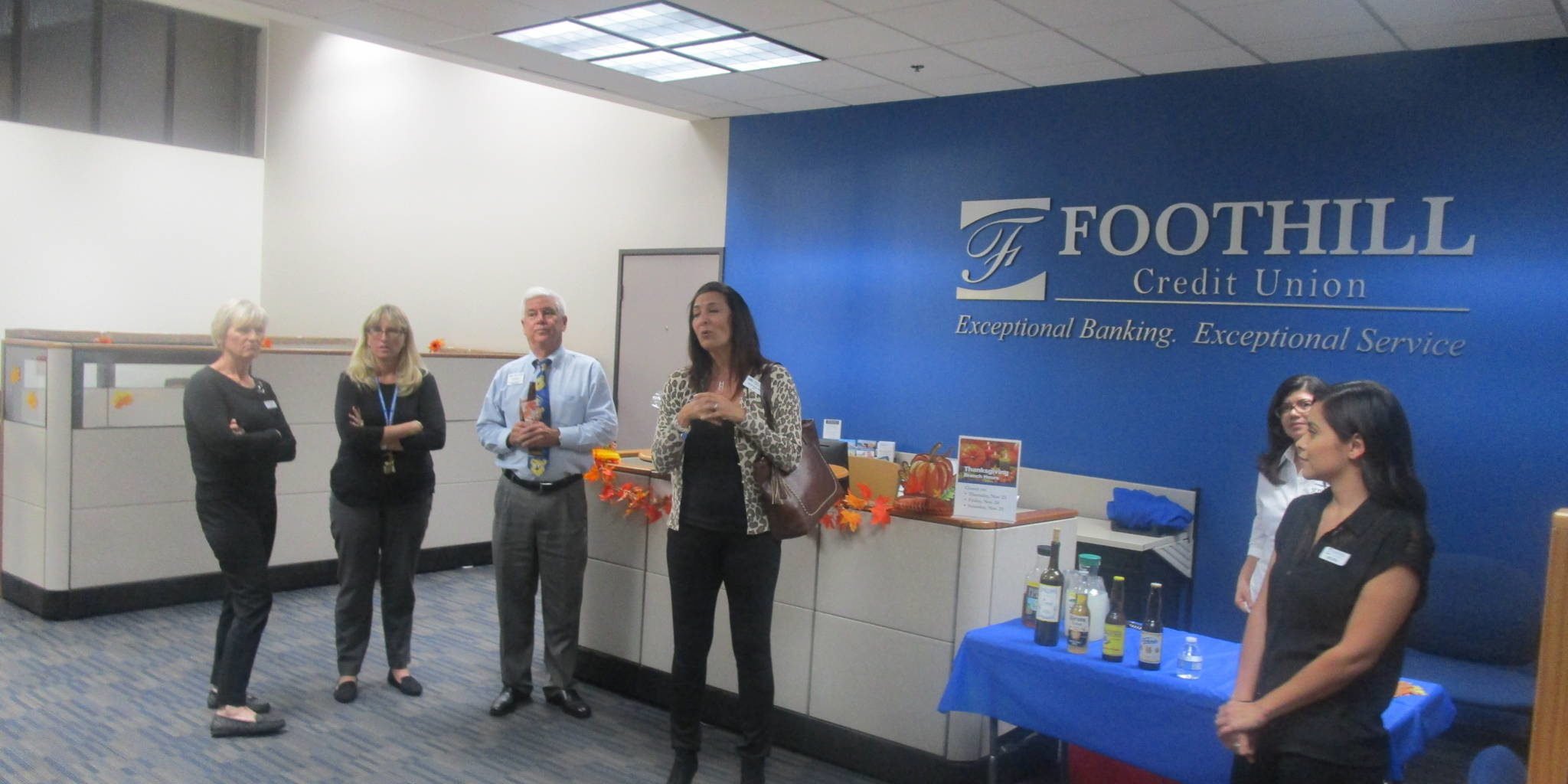 a group of people standing in front of a large blue logo for Foothill Credit Union