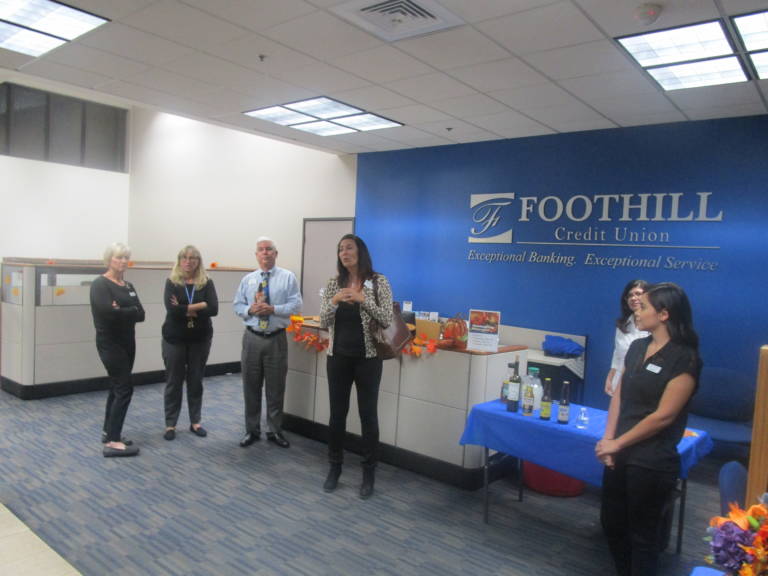 a group of people standing in front of a large blue logo for Foothill Credit Union