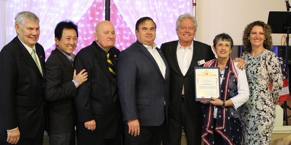 two women standing with a group of men and one of the women is holding a certificate