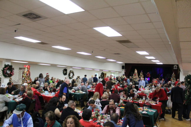 IMG_5865 a large group of people in a lodge room all dressed in christmas attire with christmas trees spread around