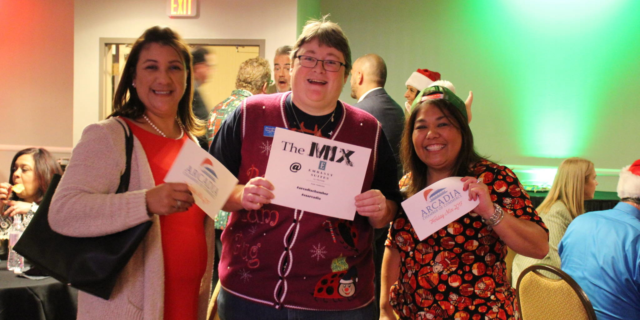 three women hold signs advertising the Arcadia Chamber mixer