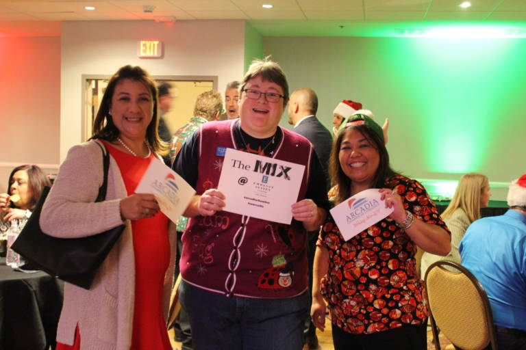 three women hold signs advertising the Arcadia Chamber mixer