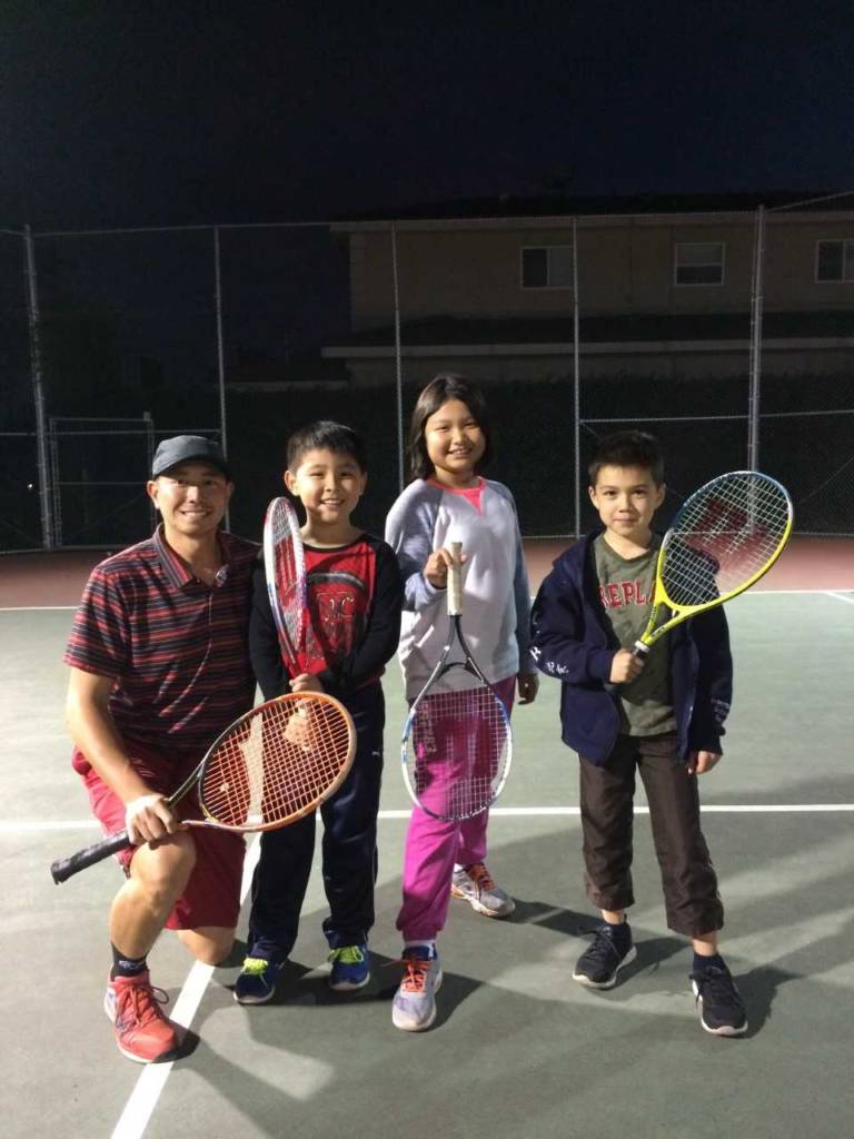 a group of kids on a tennis court with their coach