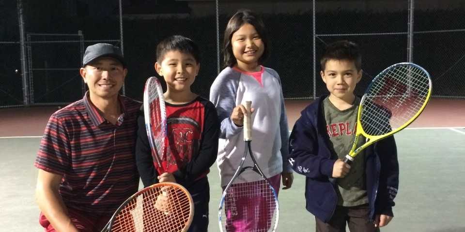a group of kids on a tennis court with their coach