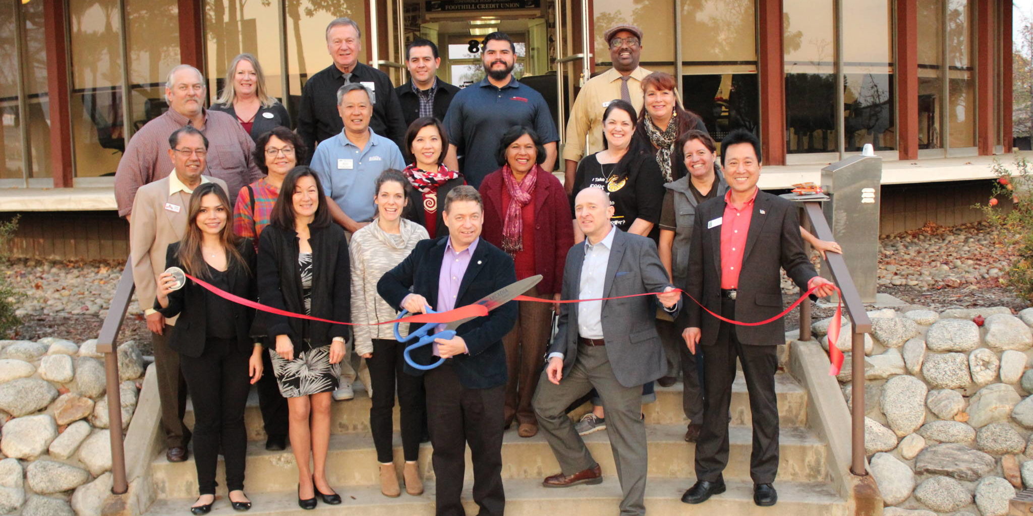 a group of people standing on the back steps of the Arcadia Chamber building and one is holding giant scissors