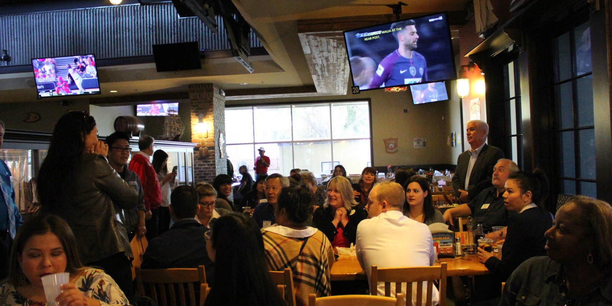 IMG_1997 a group of people in a dark restaurant setting with sports playing on TVs above their heads
