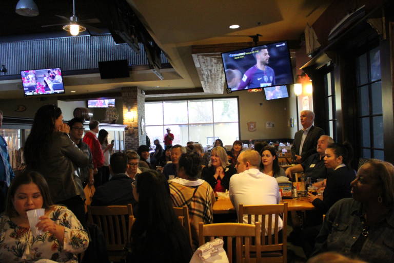 a group of people in a dark restaurant setting with sports playing on TVs above their heads
