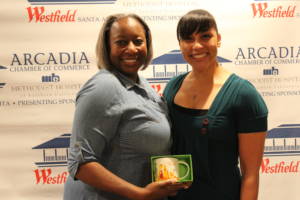 two women standing in front of a step and repeat banner holding a certificate 