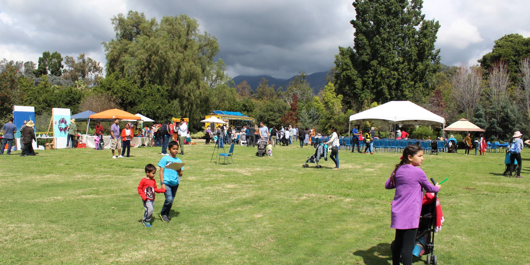 IMG_3406 a group of people at a festival with booths and umbrellas set up though the sky looks cloudy and stormy