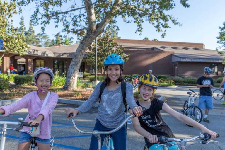 three young children on bicycles in front of a community center