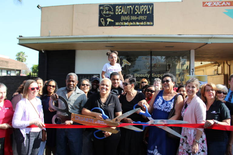 a large group of people holding a pair of giant scissors and red ribbon beneath a sign for beauty supplies