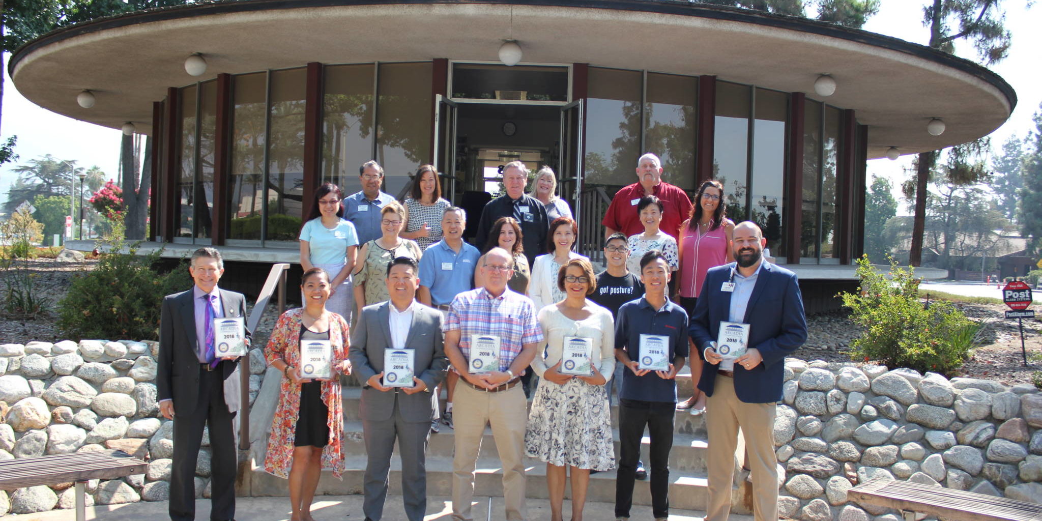 a group of people standing on the back steps of the Arcadia Chamber building holding plaques
