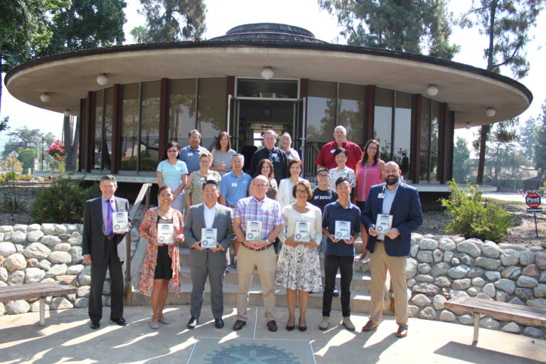 a group of people standing on the back steps of the Arcadia Chamber building holding plaques