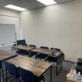 a classroom showing tables and chairs with a white wall behind them 