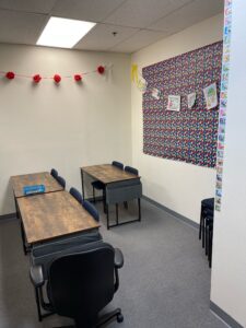 the inside of a classroom showing tables and chairs with a bulletin board on the wall 