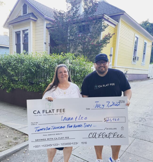 a man and woman holding an oversized check labeled CA Flat Fee standing in front of a yellow house