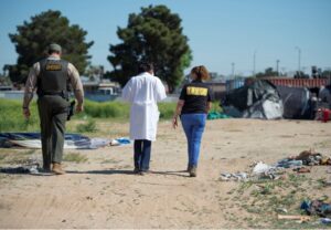 three people walking down a path in a homeless encampment