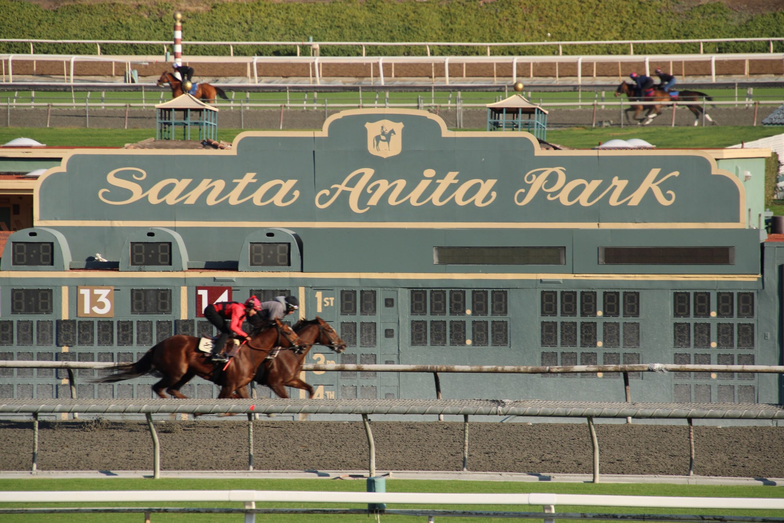 two horses running in front of the Santa Anita Park sign