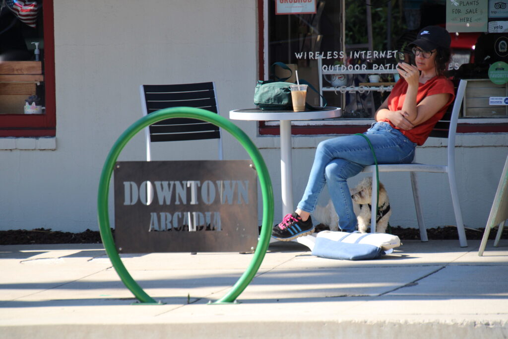 a Downtown Arcadia bikerack with a woman sitting behind it drinking coffee