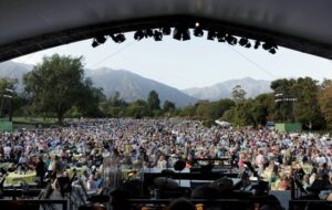 a concert crowd seen from the dome of a stage with mountains in the background 