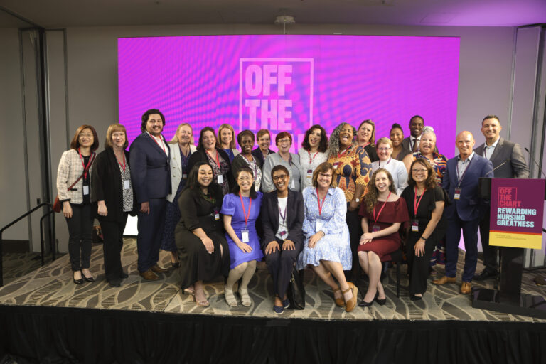 a group of people on a stage both seated and standing with a purple backdrop behind them