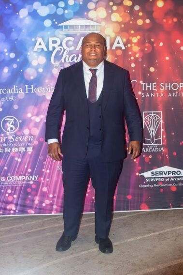 a man in a suit and tie standing in front of a colorful step and repeat banner