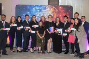 a large group of people standing in front of a colorful step and repeat banner, all holding I love Downtown Arcadia stickers