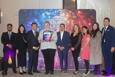 a woman holding plaques and certificates standing with a group of people in front of a colorful step and repeat banner
