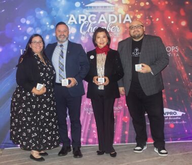 two women standing with two men all in gala attire, in front of a colorful step and repeat banner