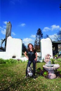 a woman in black stands in front of a destroyed home in Altadena with her down standing between her legs
