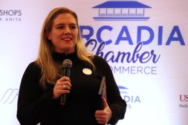 a woman in a black sweater holding a microphone and a plaque under her arm