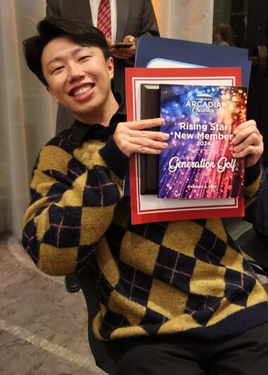 a man in a black and yellow sweater holding up a colorful plaque and smiling