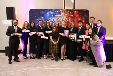 a large group of people standing in front of a colorful step and repeat, holding stickers that read I love Downtown Arcadia