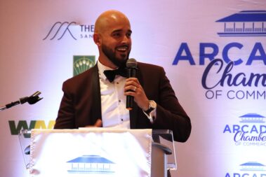 a man with no hair and a beard standing in front of a podium and holding a microphone