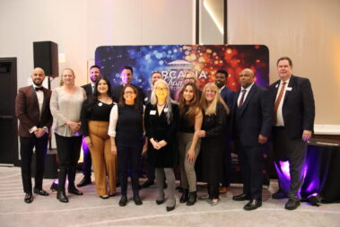 a large group of people standing in front of a colorful step and repeat