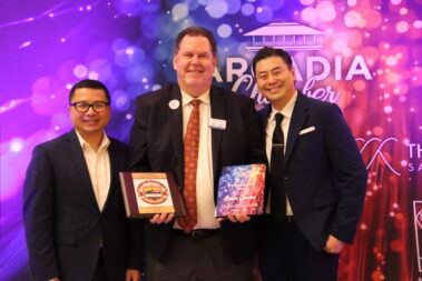 three men standing in front of a colorful step and repeat, and the one in the middle is holding plaques in each hand