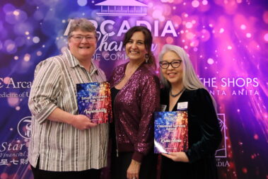 three women standing in front of a colorful step and repeat and the two on the ends are holding colorful plaques