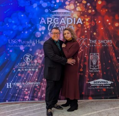 a woman in a purple dress standing with a man in a black suit, in front of a colorful step and repeat banner