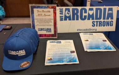 blue baseball caps set up on a table with flyers and signs that read Arcadia Strong