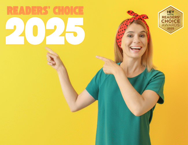 a woman in a green shirt with a red bandana on her head pointing at the words Readers Choice 2025 in the left corner, against a yellow background