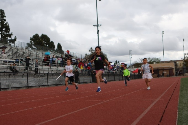 four young people compete on a track with a cloudy sky above them