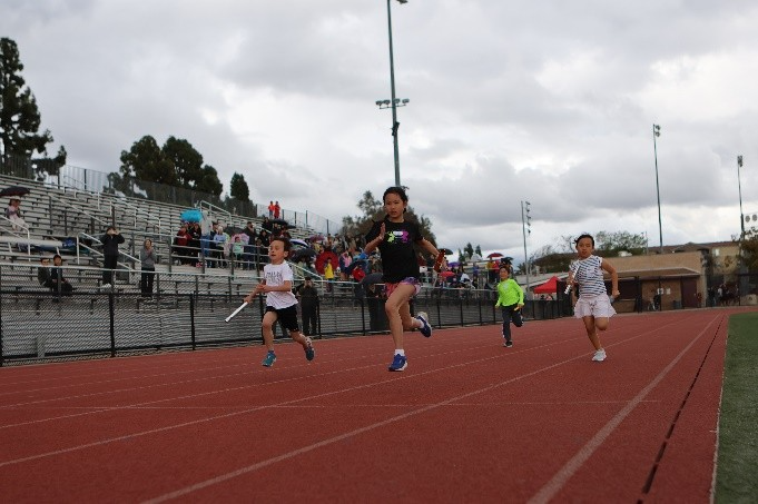 four young people compete on a track with a cloudy sky above them