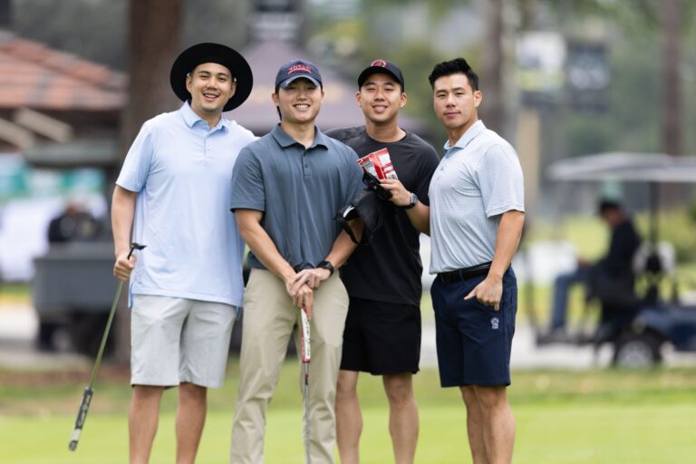 four men in golf gear pose on a golf course
