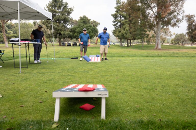 two men in blue shirts in the distance look towards at cornhole toss game