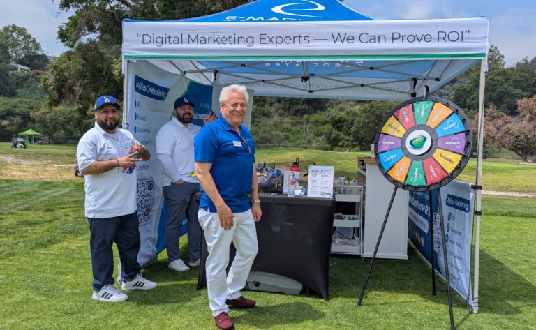 a man in blue standing in front of a booth with a spinning wheel, with E-Marketing Associates